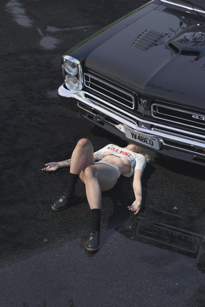 A woman in a crop top with the words 'KILL YOU' is lying face-down on a wet asphalt parking lot with a vintage black car positioned over her.